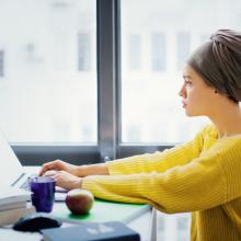 一个戴着头巾和黄色毛衣的女人在电脑上工作